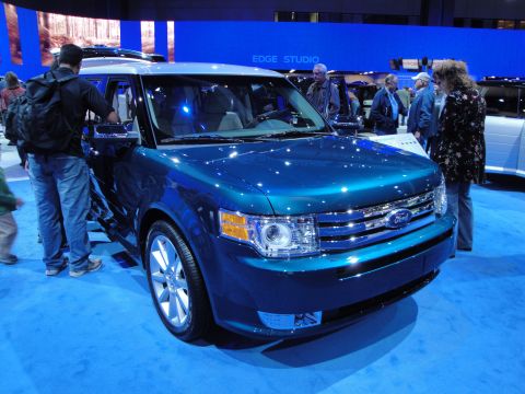 1993 Ford Taurus - Blue Ford Flex SUV displayed at an auto show with people looking at it.