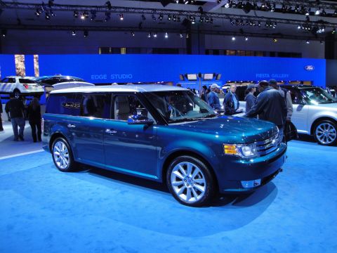 1993 Ford Taurus - Blue Ford Flex SUV displayed at an auto show with other vehicles and attendees present.
