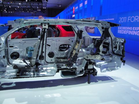 1993 Ford Taurus - Chassis cutaway of a vehicle on display, with a red SUV in the background. Text indicates '2011 Ford'.