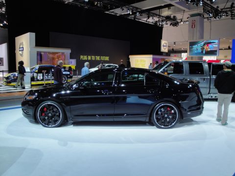 1993 Ford Taurus - A black sedan with custom wheels is displayed at an auto show next to a pickup truck.