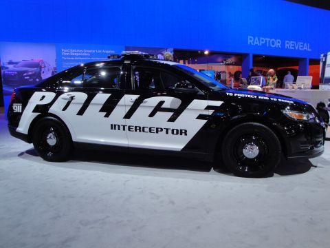 1993 Ford Taurus - This police interceptor car, likely a modern Ford Taurus, is displayed indoors with "RAPTOR REVEAL" visible in the background.