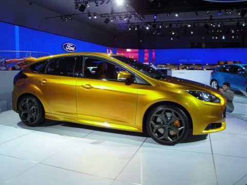 1993 Ford Taurus - Gold hatchback on display at an auto show with a blue car and a person in the background.