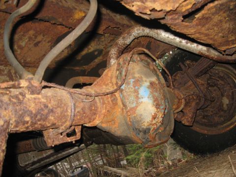 1981 Ford Bronco - Underside view of a severely rusted vehicle's rear axle and suspension components.