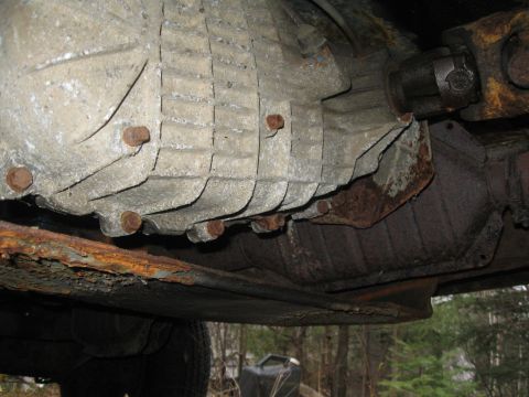 1981 Ford Bronco - The underside of a vehicle reveals a heavily rusted transmission and driveshaft assembly.