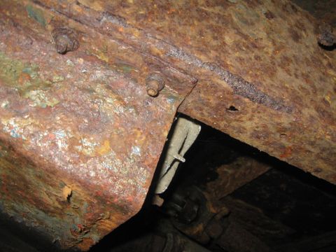 1981 Ford Bronco - Close-up view of heavily rusted undercarriage components, with visible bolts and some peeling paint.