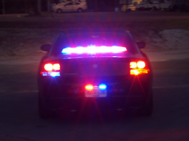 Rear of dark Dodge Charger at night with red and blue police lights flashing