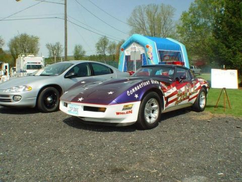 1991 Ford LTD Crown Victoria - A Chevrolet Corvette is decorated as a police car with patriotic graphics and emergency lights.