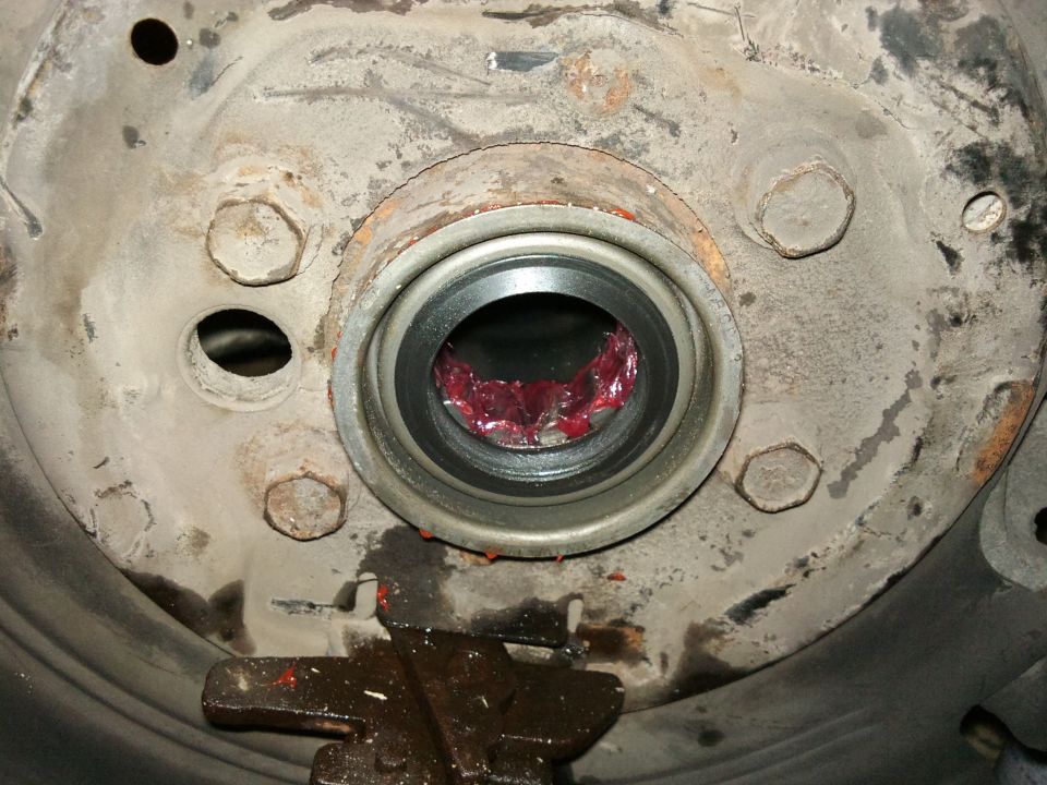 Close-up of a wheel bearing assembly packed with red grease, showing bolts and a rusty metal surface