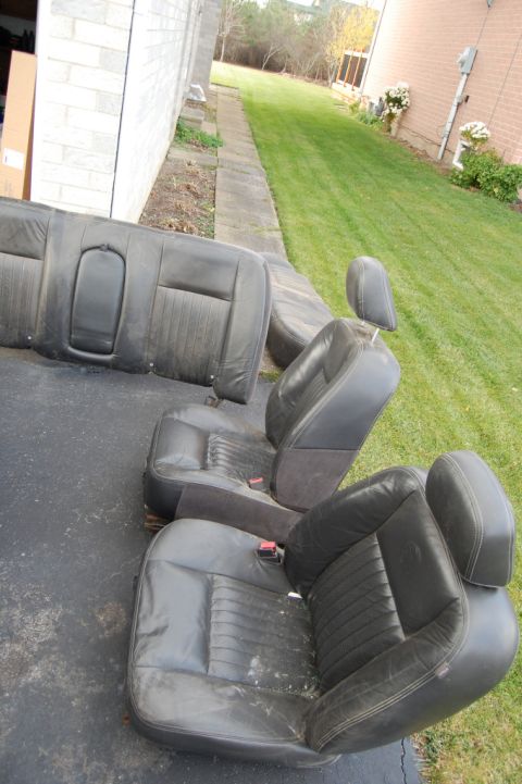 1985 Mercury Grand Marquis - Car seats are laid out on the ground next to a building and a lawn.