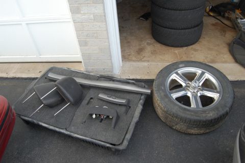 1985 Mercury Grand Marquis - Interior car parts and a spare tire are organized on the ground next to a garage door.