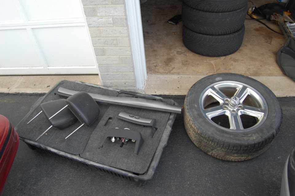 Car interior parts, including headrests and a control panel, are laid out next to a spare tire. Stacked tires are visible in the background