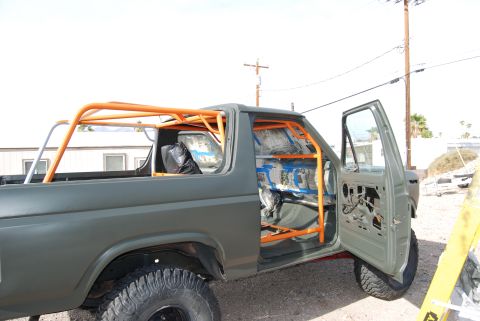 1982 Ford Bronco - This modified SUV features an extensive orange roll cage, with the driver's side door open and interior removed.