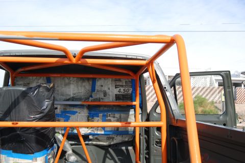 1982 Ford Bronco - The interior of a vehicle is visible, covered in an orange roll cage and newspaper.