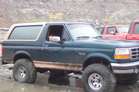 1995 Ford Bronco - This Ford Bronco is shown off-road in muddy conditions, with another vehicle partially visible in the background.