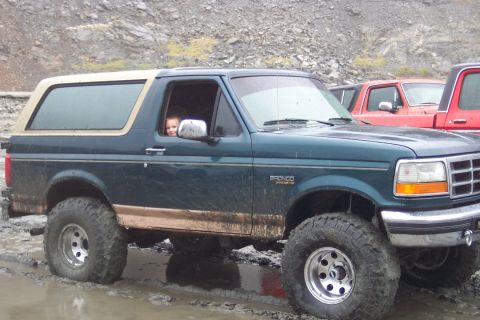 1995 Ford Bronco - A dark green Ford Bronco with tan trim is stuck in mud, with other trucks visible behind it.