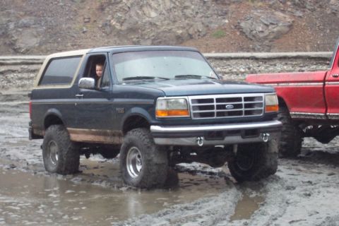 1995 Ford Bronco - 1995 Ford Bronco navigating a muddy off-road course next to a red pickup truck.