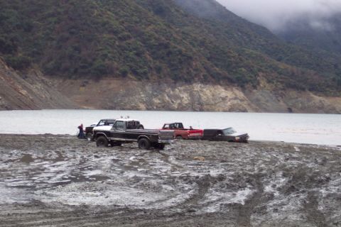 1995 Ford Bronco - Multiple trucks are bogged down in the mud by the water's edge.
