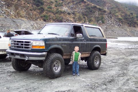 1995 Ford Bronco - A young boy stands next to a modified Ford Bronco in a rocky, outdoor setting.