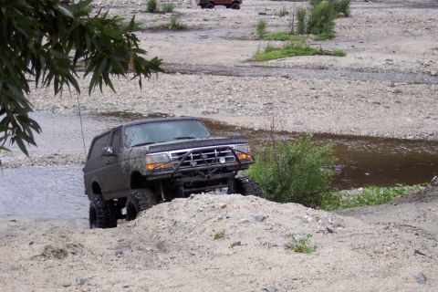 1995 Ford Bronco - Mud-covered 1995 Ford Bronco navigates a challenging off-road course in a dry riverbed.