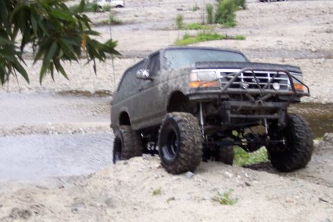 1995 Ford Bronco - This heavily modified SUV, likely a 1992 model, is shown off-roading in a dirt and water environment.