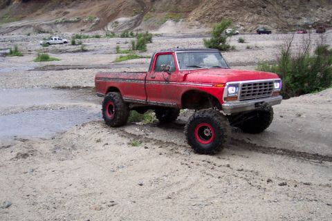 1995 Ford Bronco - This lifted red pickup truck is equipped for off-road driving in a rocky, dry riverbed.