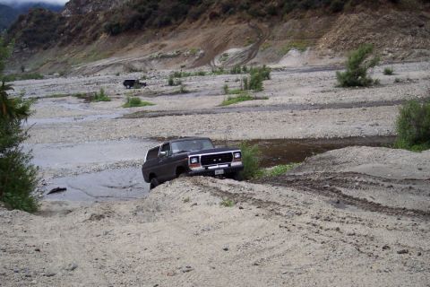 1995 Ford Bronco - A dark 1979 Ford Bronco navigates a rocky, dry riverbed with another SUV visible in the distance.