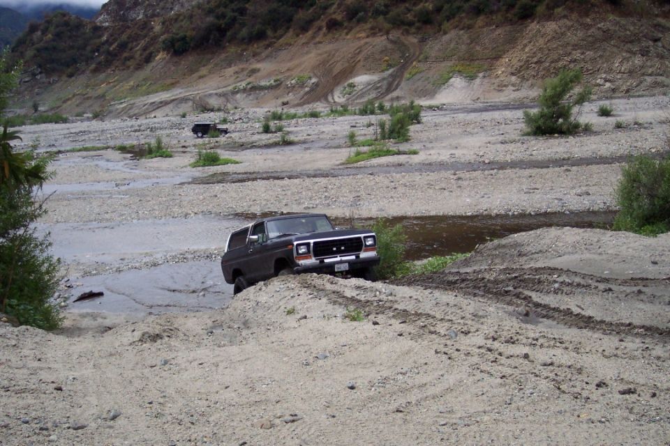 Dark SUV on dirt mound near water, with another SUV in background