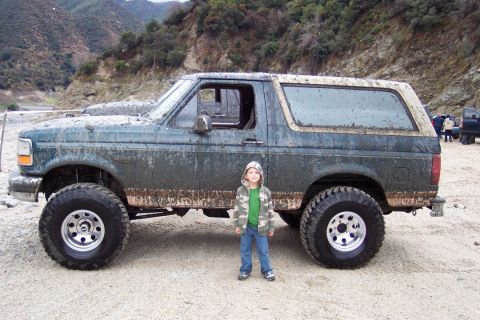 1995 Ford Bronco - Muddy 1995 Ford Bronco in an outdoor, off-road setting with a child posing beside it.