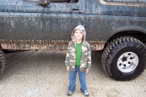 1995 Ford Bronco - A young child poses next to a heavily mud-splattered SUV.
