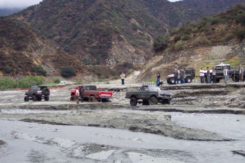 1995 Ford Bronco - A group of off-road vehicles traverse a challenging, dry riverbed in a mountainous area.
