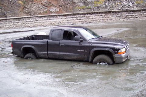 1995 Ford Bronco - A black Dodge Dakota pickup truck is stuck deep in mud, with its wheels submerged.