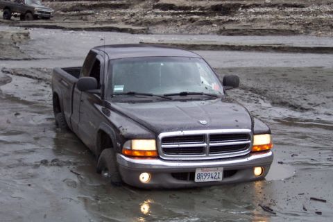 1995 Ford Bronco - A dark pickup truck is stuck in muddy terrain, with another vehicle in the background.