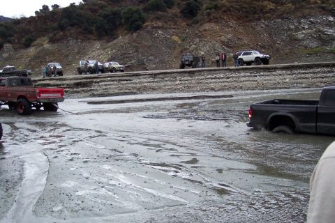 1995 Ford Bronco - Multiple off-road vehicles navigate a challenging muddy path, with some appearing to be stuck.