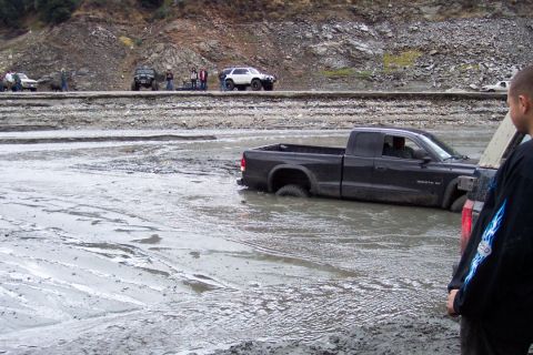 1995 Ford Bronco - Several vehicles are present in a muddy area, with one black pickup truck deeply stuck in the mire.