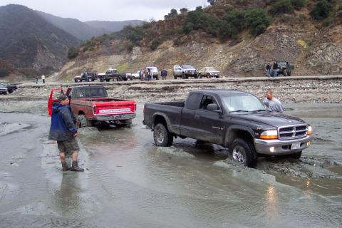 1995 Ford Bronco - A black Dodge Dakota navigates a muddy terrain, with other trucks visible in the background.