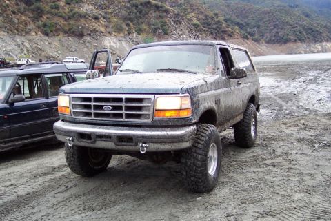 1995 Ford Bronco - A muddy Ford Bronco sits off-road with another vehicle nearby.