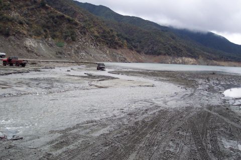 1995 Ford Bronco - Multiple vehicles navigate a muddy, watery terrain with mountains in the background.