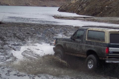 1995 Ford Bronco - A 1995 Ford Bronco navigates a muddy, watery terrain, kicking up spray.
