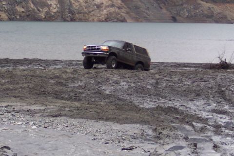 1995 Ford Bronco - Ford Bronco navigating challenging muddy terrain beside a body of water.