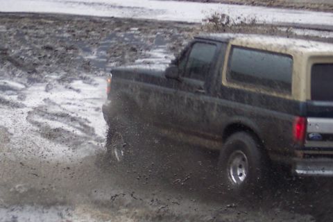 1995 Ford Bronco - A muddy Ford Bronco navigates a wet, off-road terrain.