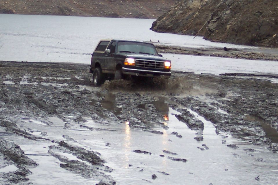 Dark green 1995 Ford Bronco driving through mud