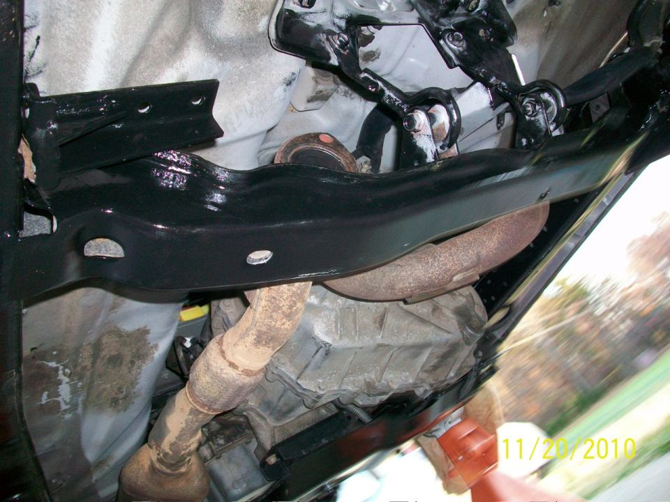 Underside view of vehicle showing exhaust pipes, catalytic converter, and transmission housing. Black painted frame components are visible