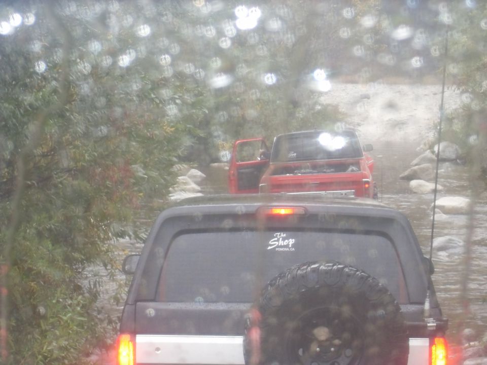 Dark SUV rear view with spare tire, followed by red pickup truck with open hood