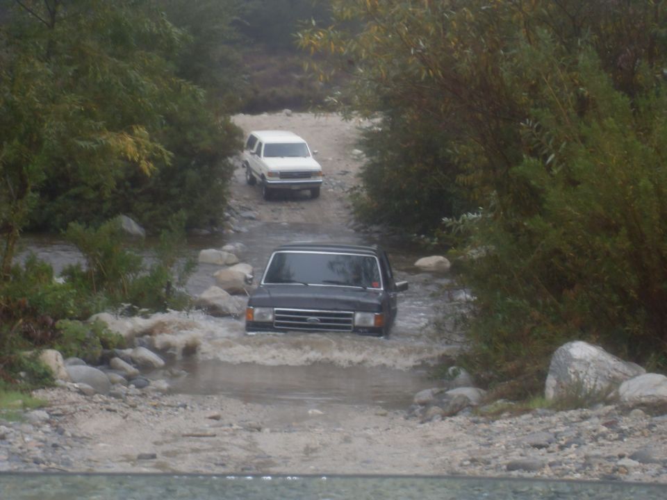 Dark SUV driving through water, white SUV behind it on a dirt path