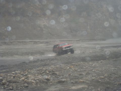 1979 Ford Bronco - A red SUV navigates a rough terrain, kicking up dust as it drives through a desolate landscape.