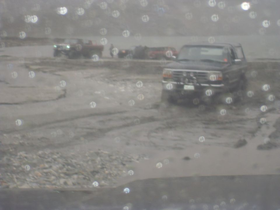 Dark SUV with a prominent grille and front bumper, stuck in mud