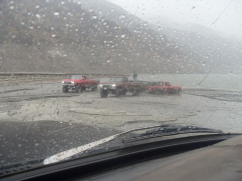 1979 Ford Bronco - Multiple trucks are stuck in a muddy area, possibly after rain or near water.