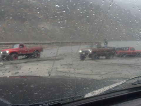 1979 Ford Bronco - Multiple trucks and an SUV navigate a wet, muddy road in overcast conditions.