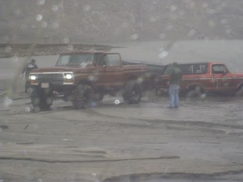1979 Ford Bronco - Two trucks are stuck in the mud, with people nearby.