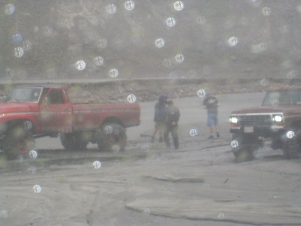 Red pickup truck and maroon SUV in a sandy, outdoor area with people